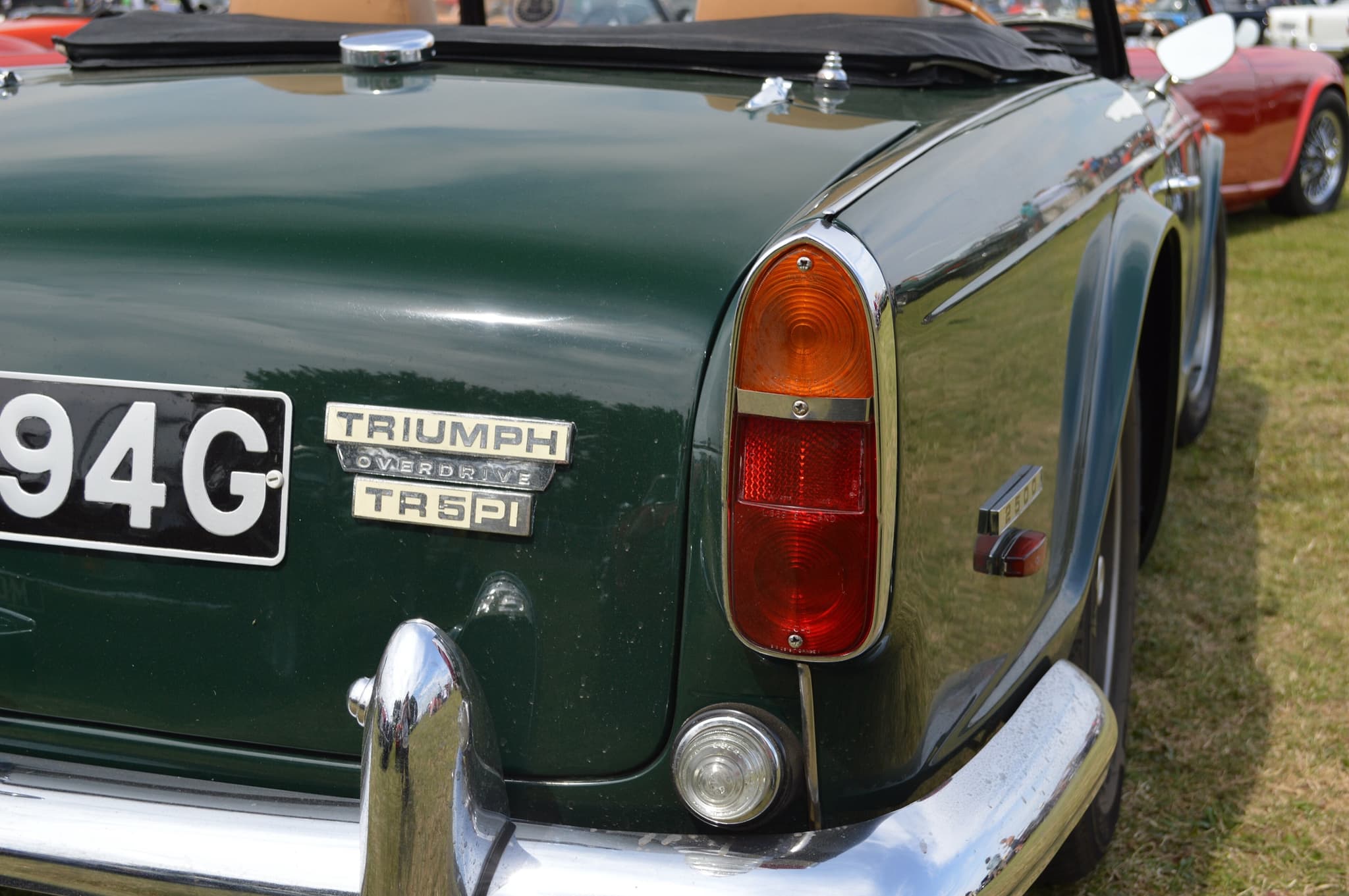 Close-up of a dark green boot with chrome TRIUMPH, OVERDRIVE and TR5 PI badges beside a tail lamp and reversing lamp.