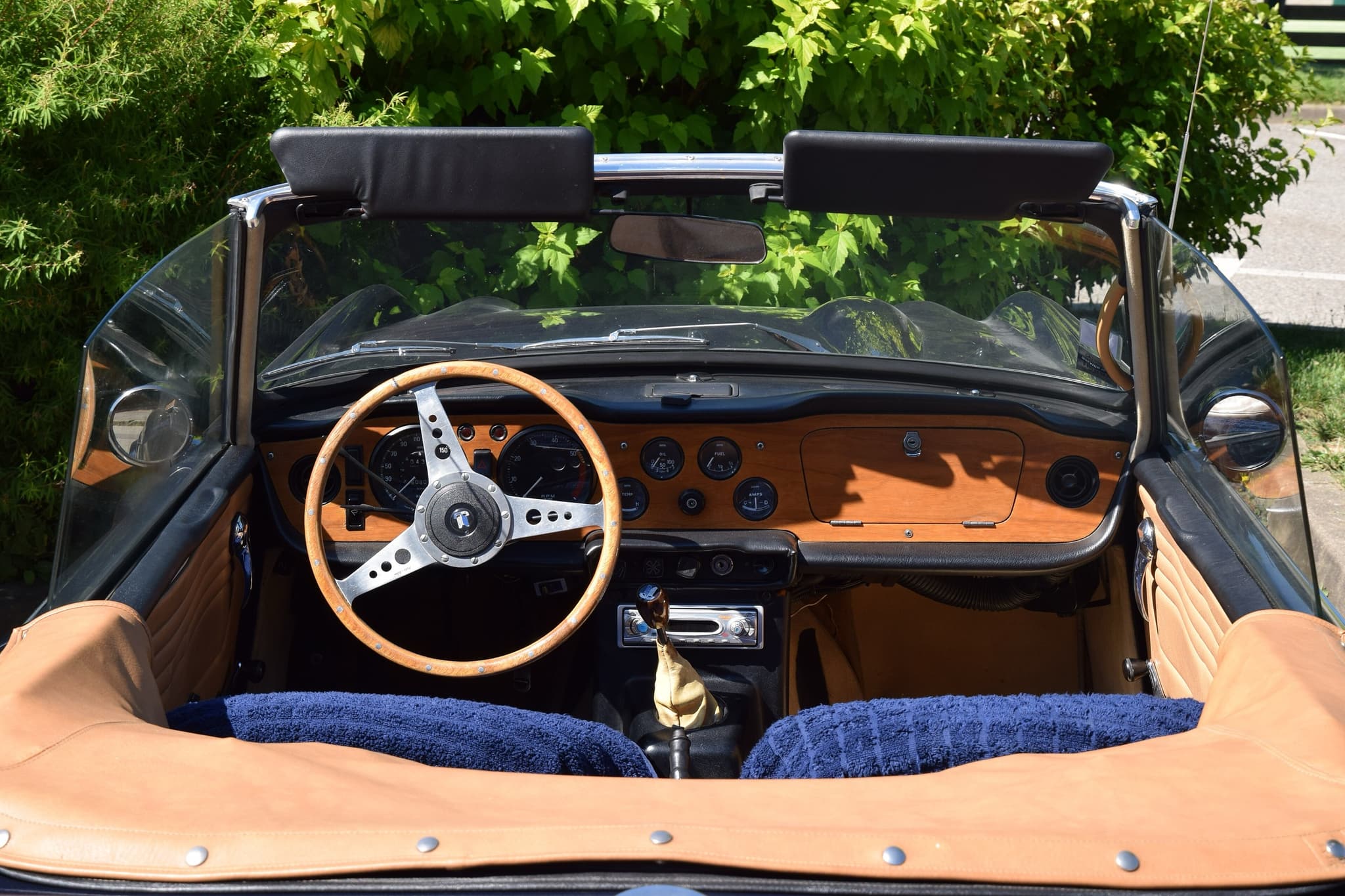 The cockpit of an open sports car seen over its folded hood cover: a wooden dashboard with round gauges and a wood-rimmed wheel.