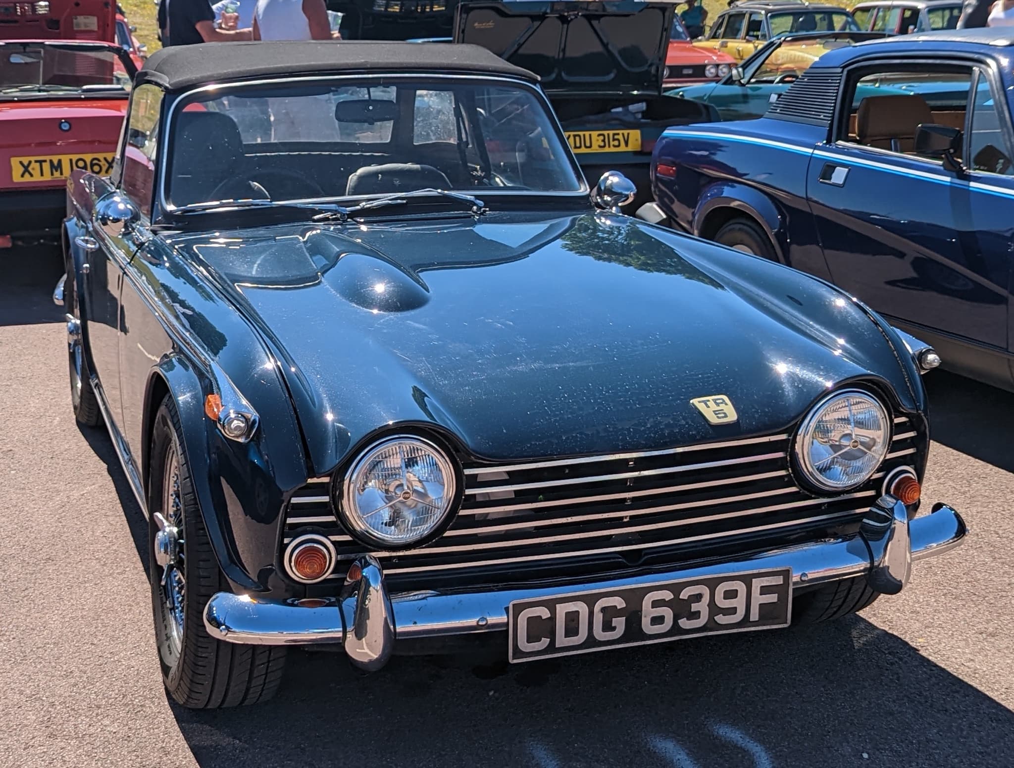 A dark blue sports car with its black hood up and wire wheels, seen nearly head-on at a club show.