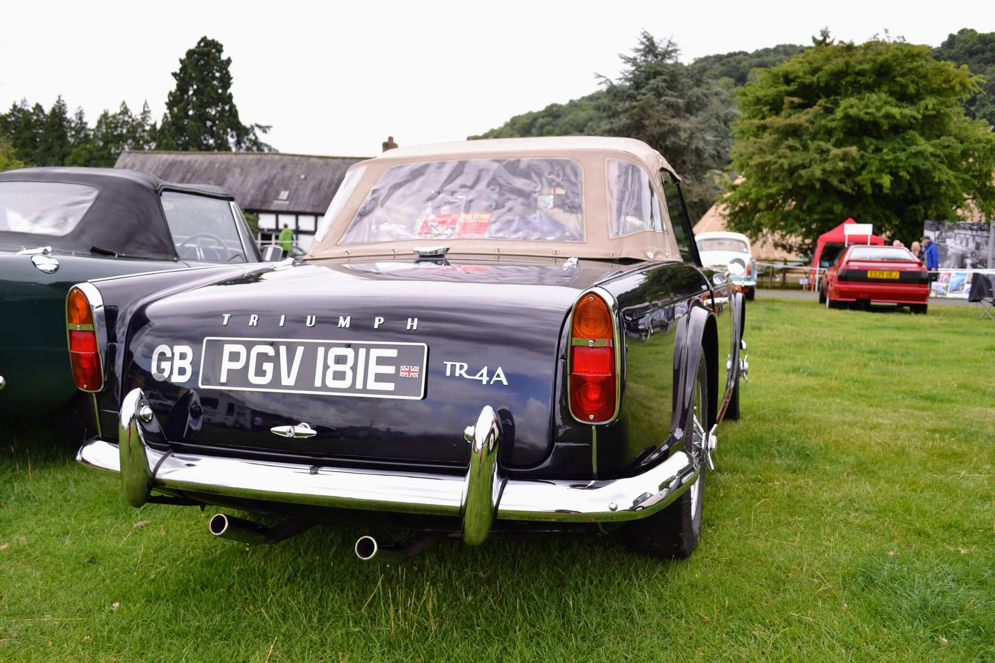 A dark blue Triumph TR4A with a beige hood up, seen from behind on the grass paddock of a hill-climb.