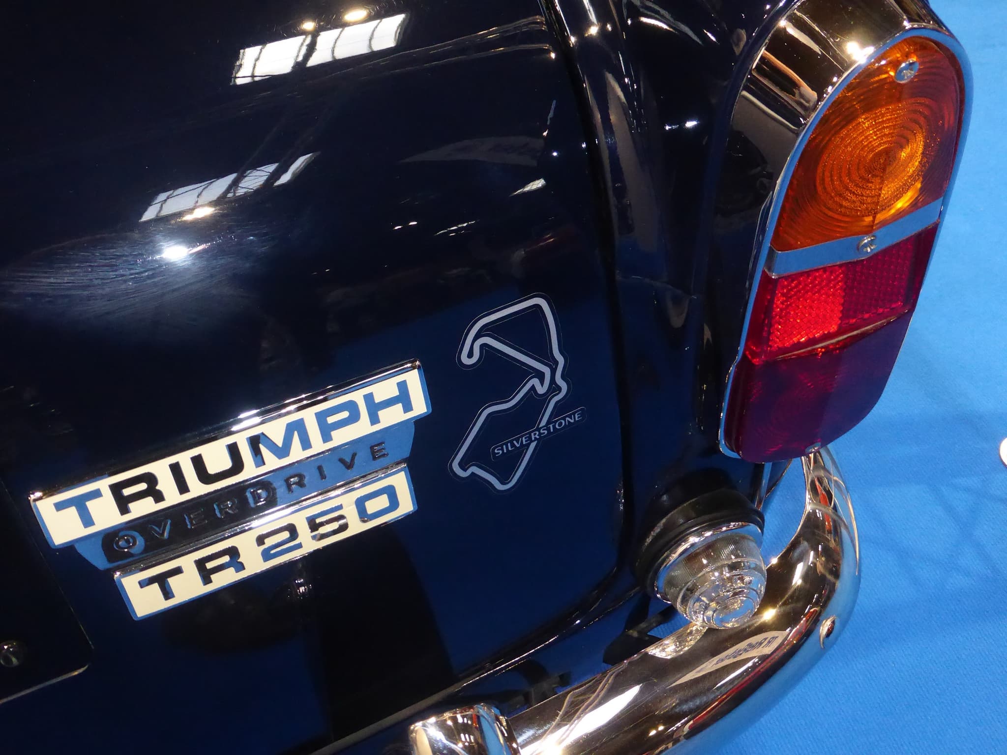 Close-up of a dark blue boot with chrome TRIUMPH, OVERDRIVE and TR250 badges beside a tail lamp.